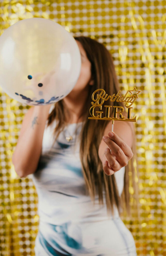 Woman holding a "Birthday Girl" sign with a balloon in front of her face