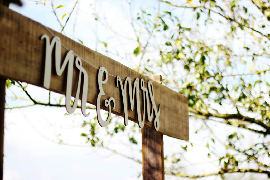 Rustic "Mr & Mrs" sign on a wooden frame, with trees in the background