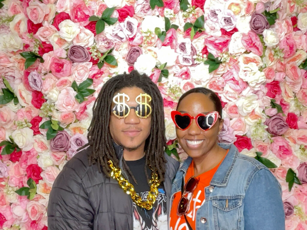 Two guests with props on a photo booth with floral background