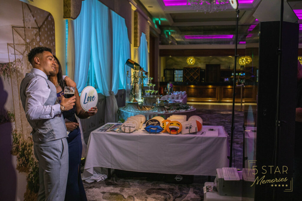 A couple posing for photos on the photo booth in front of a backdrop using props